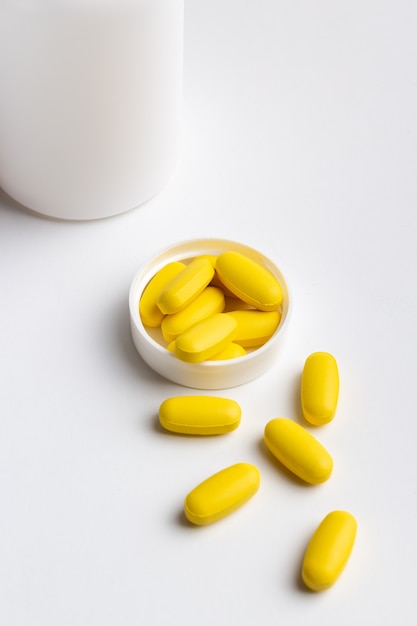 желтые таблетки и бутылка, изолированные на белом фоне