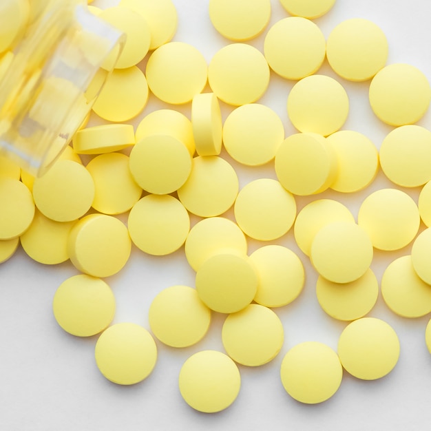 Yellow pills scattered from a glass jar on white 