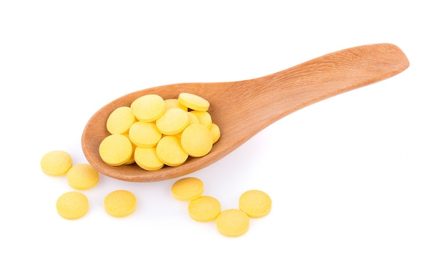 Yellow pills in spoon isolated on white surface