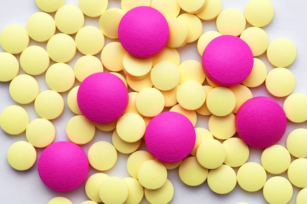 Желтые и розовые таблетки на белом фоне.