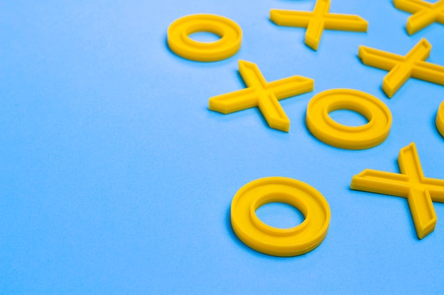 Yellow plastic crosses and zeroches for playing tic-tac-toe on a blue surface. Concept XO Win Challenge. Educational game for kids