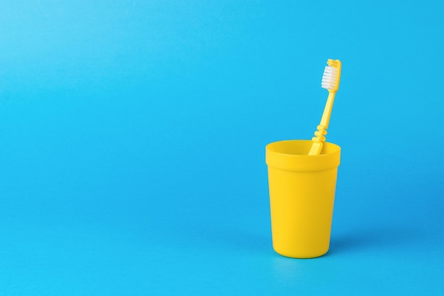 A yellow plastic cup with a yellow toothbrush on a blue background