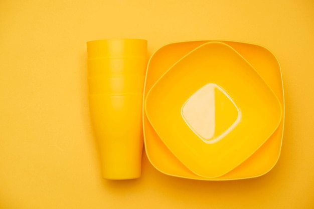 Bicchieri e piatti di plastica gialli su sfondo giallo. utensile da cucina. vista dall'alto. stile minimalista. copia, spazio vuoto per il testo