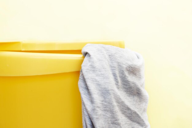 Yellow plastic laundry basket with gray clothing on a yellow background