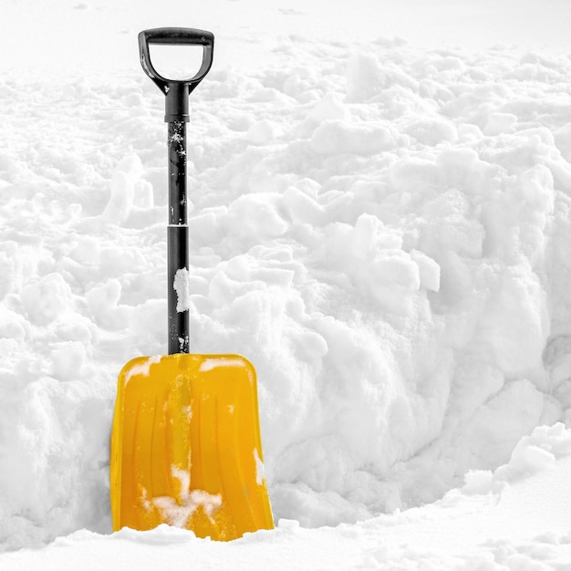 Желтая пластиковая лопата зимой застряла в пушистом белом снегу