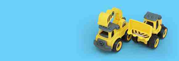 Photo yellow plastic truck and bulldozer toy isolated on blue background with copy space for text or banner
