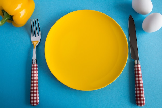 Yellow plate,fork,knife and  ingredients for breakfast  on the blue  background.Top view.