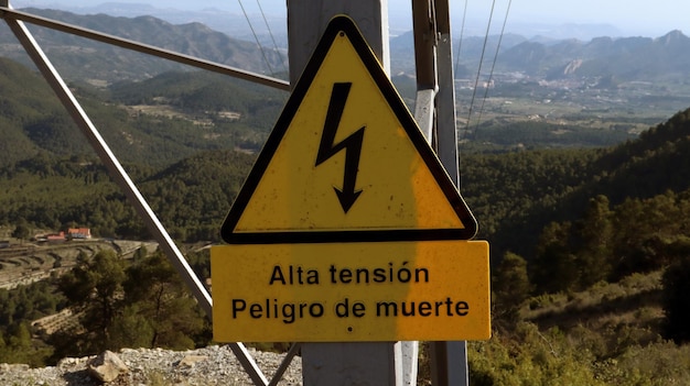 Yellow plate on the power line. Hazard warning in Spanish Peligro de muerte. Drawn lightning