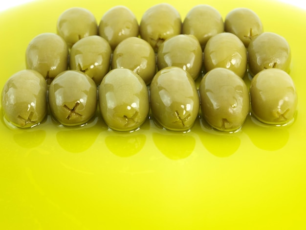 A yellow plate with green olives on it and a small x on the bottom