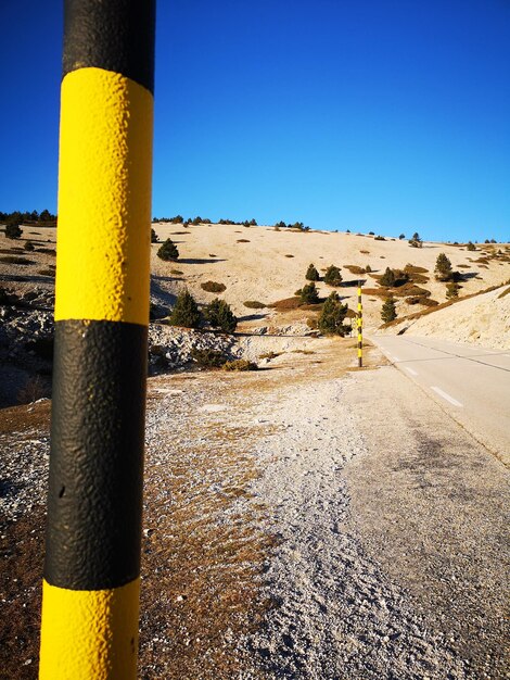 Yellow pole on road by land against clear blue sky