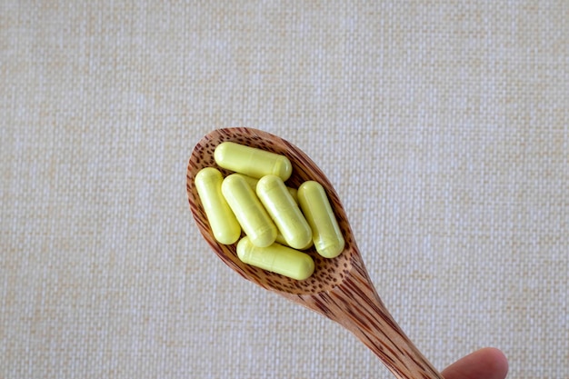 Yellow quercetin capsules in a wooden spoon on a beige background Dietary supplement vitamin or tablet closeup view from above Treatment of allergies asthma