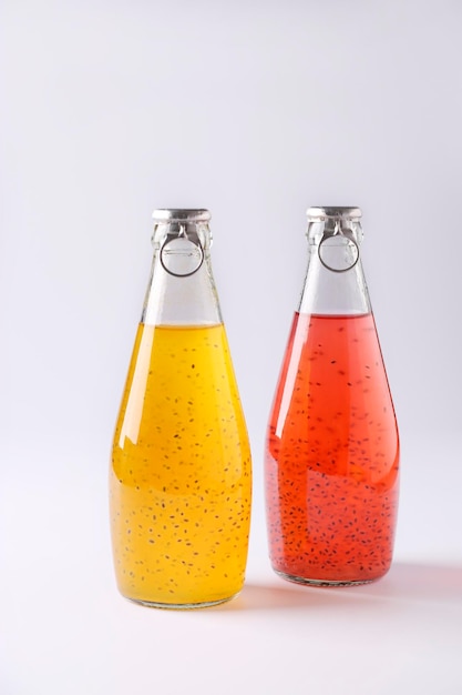 Yellow and red drinks with basil seeds or falooda seeds or tukmaria in bottles on white background