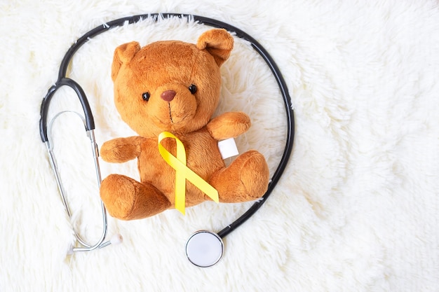 Photo yellow ribbon on bear doll with stethoscope on white background for supporting kid living and illness. september childhood cancer awareness month and world cancer day concept