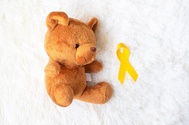 Yellow Ribbon with Bear doll on white background for supporting kid living and illness. September Childhood Cancer Awareness month and World cancer day concept