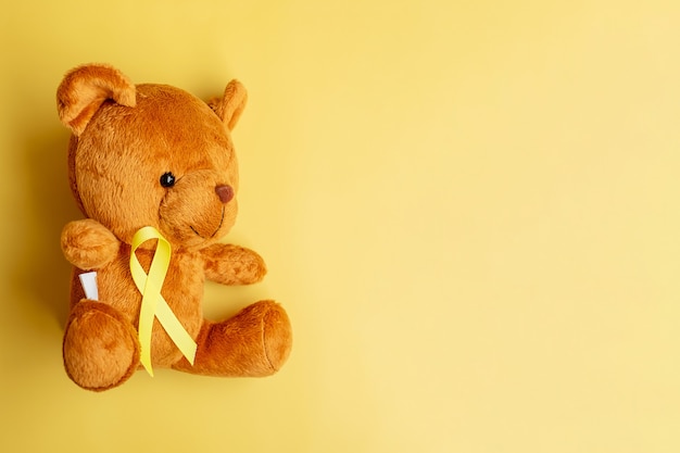 Yellow Ribbon with Bear doll on yellow color background for supporting kid living and illness. September Childhood Cancer Awareness month and World cancer day concept