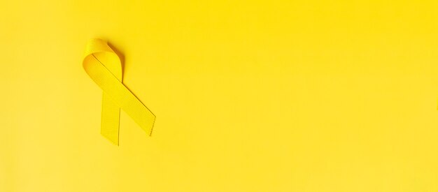 生きている人々と病気をサポートするための黄色の背景に黄色いリボン。 9月の自殺予防デー、小児がん啓発月間、世界対がんデーのコンセプト