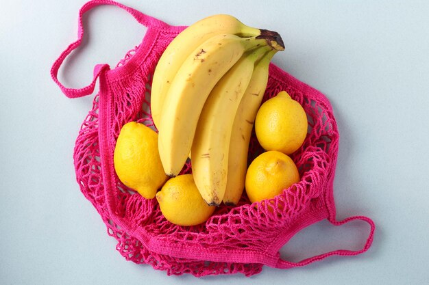 Yellow ripe bananas and lemons in fuchsia colors string mesh bag on light background