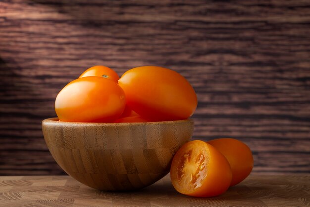 Yellow ripe tomatoes in a wooden bowl on wooden