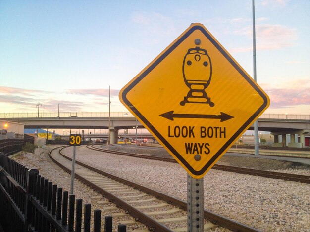 Photo yellow road sign by railroad tracks against sky