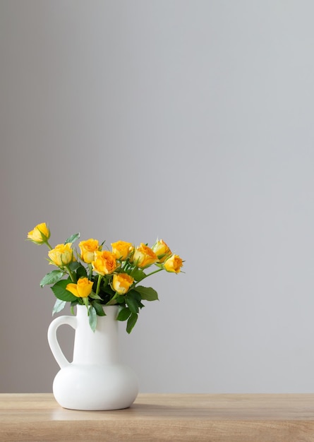 Yellow roses in white jug on wooden shelf