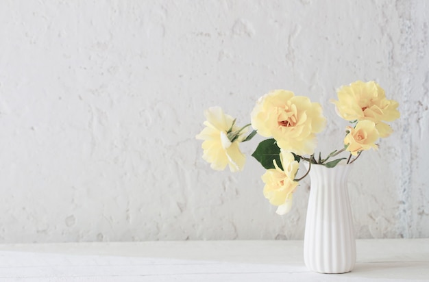 Yellow roses in white vase on background white wall