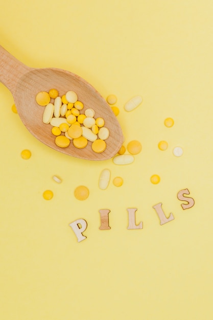 Yellow round vitamin pills in spoon on a yellow wall, copy space