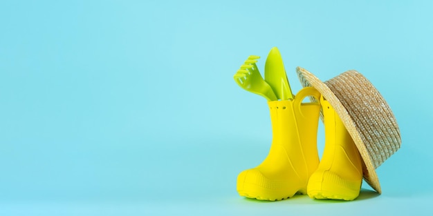 Yellow rubber boots garden tools and straw hat Gardening concept Copy space