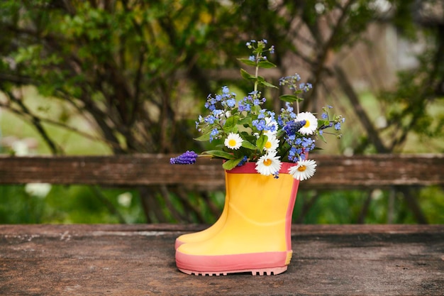 Yellow rubber boots with spring flowers bouquet on rough rural wooden background Natural background