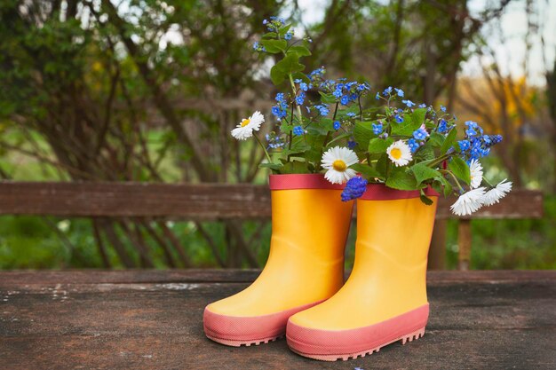 Yellow rubber boots with spring flowers bouquet on rough rural\
wooden background natural background