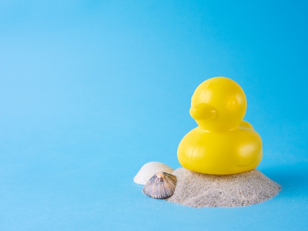 Yellow rubber duck on sand with seashells