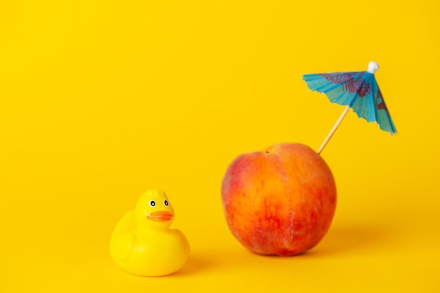 Желтая резиновая утка с персиком и зонтиком на желтом персике концепции отпуска в виде острова