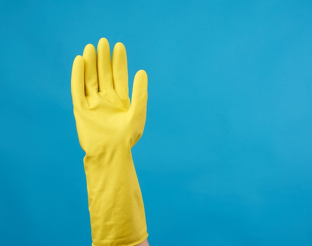 Yellow rubber glove for cleaning dressed on a female hand blue background