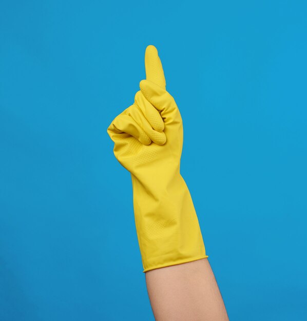 Photo yellow rubber glove for cleaning dressed on a female hand, blue background