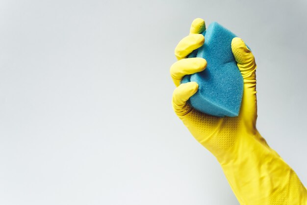 Yellow rubber glove is holding sponge on white