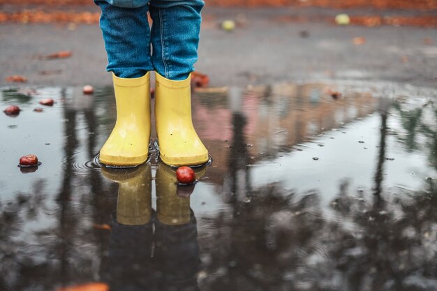 Yellow rubber shoes in puddle after raining. Falling leaves. Autumn season concept.