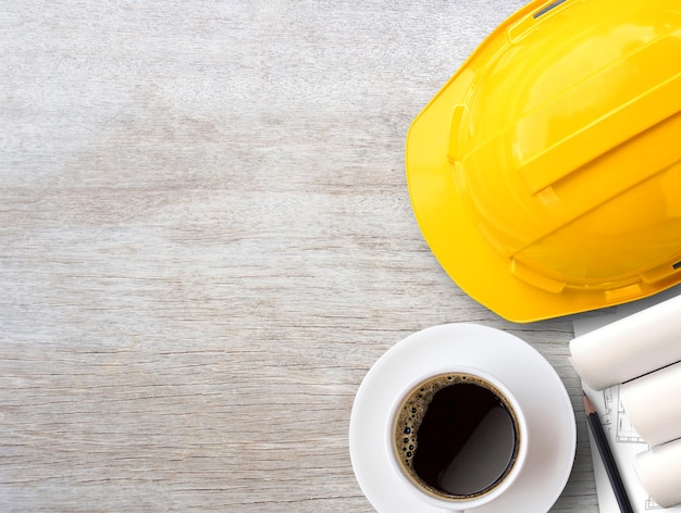 Yellow safety helmet or hard hat and construction paper plans on wood table background