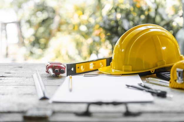 Foto casco di sicurezza giallo e disegni architettonici arrotolati su una scrivania di legno