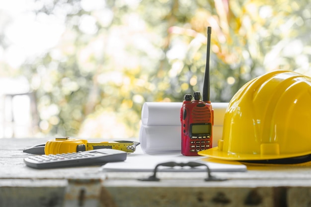 yellow safety helmet and rolled up architectural blueprints on a wooden desk