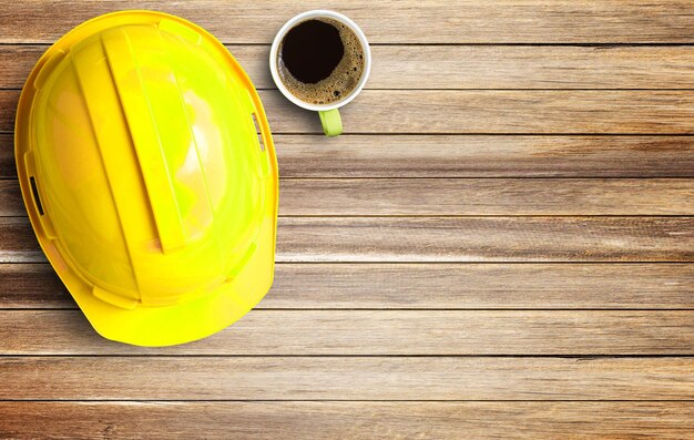 Yellow safety helmet and white paper on brown old wood background