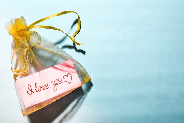 Photo yellow satin bag with a piece of pink paper and the inscription i love you on a blue background