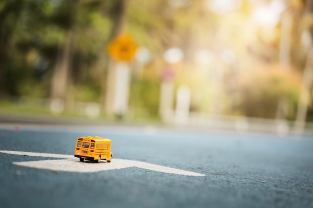 Yellow school bus toy model on country road.