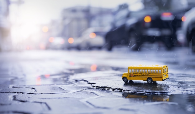 激しい雨の中に黄色のスクールバス（おもちゃのモデル）は、都市、低角度のビュー、フィールド構成の浅い深さに落ちます。学校の概念の背景に戻る。