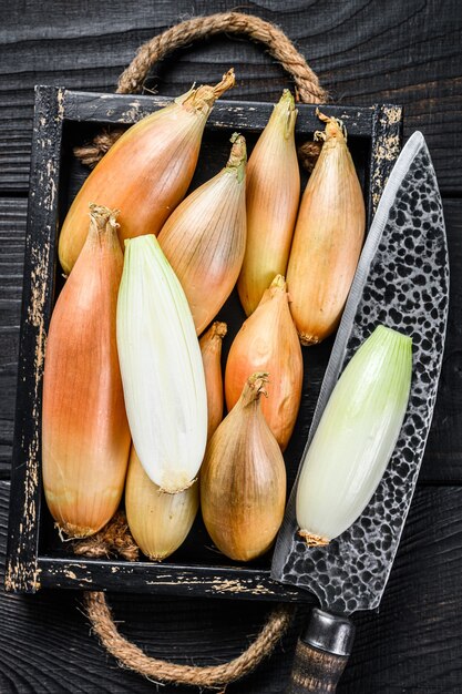 Yellow shallot onions, cut in two halves in a wooden box. Black wooden background. Top view.