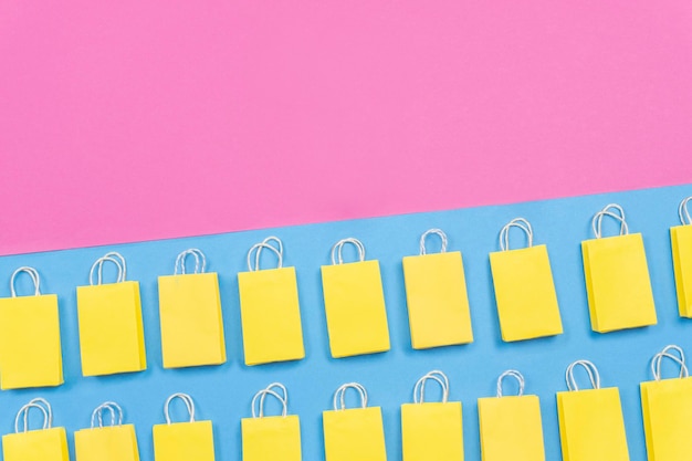 노란색 쇼핑백은 분홍색과 파란색 배경 쇼핑 개념에 평평하게 놓여 있습니다