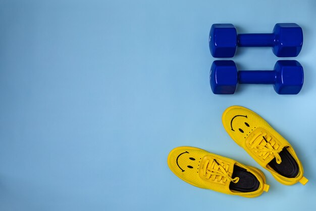 Yellow sneakers and blue dumbbells on a light blue background with copy space