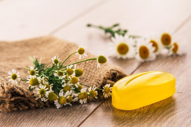 Yellow soap on sackcloth with bouquet of fresh chamomiles on wooden boards