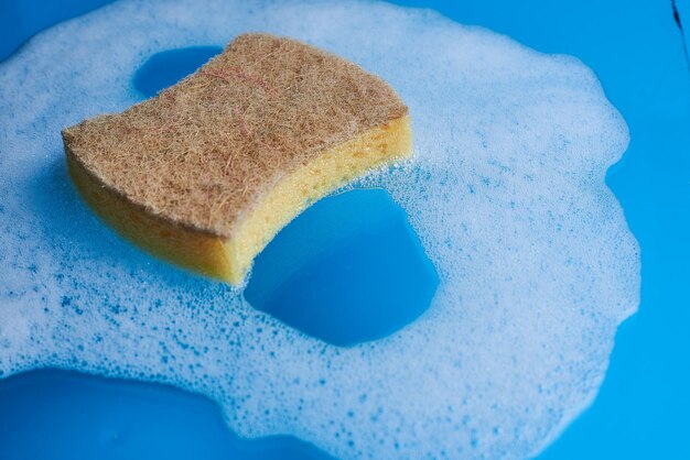 Photo yellow soapy sponge with foam on blue background cleaning concept copy space