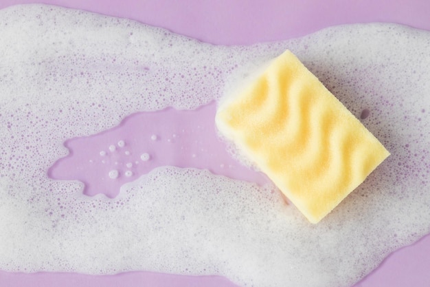 Yellow sponge with detergent foam on pink background close up Cleaning concept