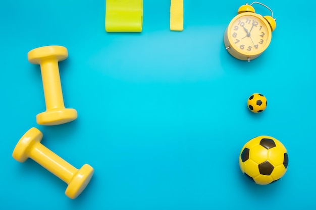 Yellow sports items dumbbells balls elastic bands for sports alarm clock on a blue background