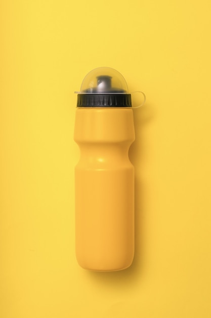 Желтая спортивная бутылка с водой на желтом фоне. Фитнес-аксессуары.